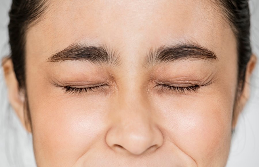 Primer plano de una mujer con los ojos fuertemente cerrados, realizando uno de los pasos de la relajación progresiva de Jacobson enfocado en la tensión facial controlada.