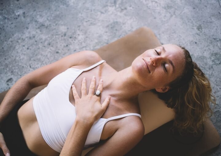 Mujer practicando un ejercicio de respiración diafragmática acostada boca arriba, con una mano sobre el pecho para sentir el movimiento respiratorio.
