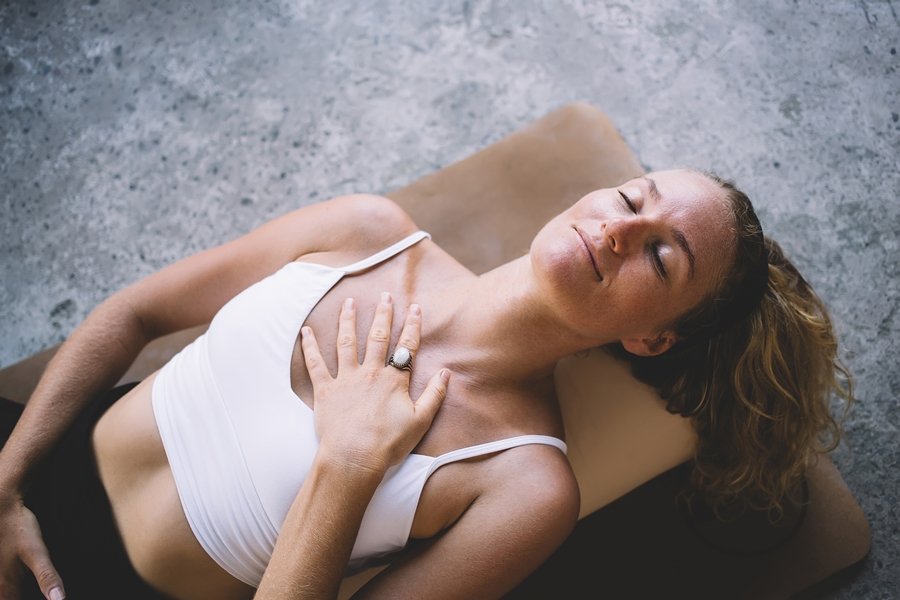 Mujer practicando un ejercicio de respiración diafragmática acostada boca arriba, con una mano sobre el pecho para sentir el movimiento respiratorio.